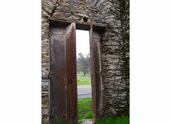Inside an old roofless rock building, looking out the old metal doors.